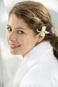 Pretty woman wearing white terry robe with white orchid flower in hair