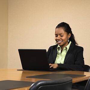 Businesswoman sitting at conference table smiling and typing on laptop computer