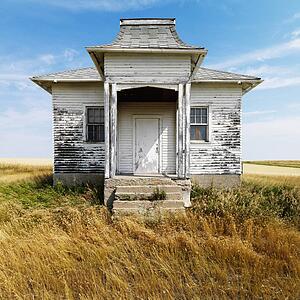 Facade of weathered abandoned building with peeling paint in grasslands.