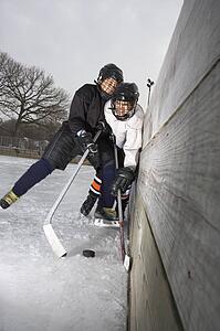 Ice hockey player boy slamming other player into wall trying to get to puck