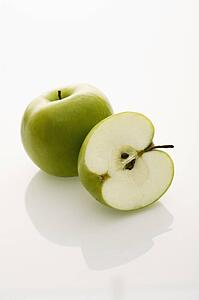 Still life of whole and sliced green apples on white background.