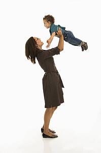 Side view of a mom lifting happy toddler son into air above head