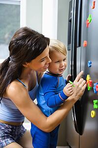 Toddler boy and mother playing with magnets on refrigerator