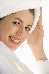 Mid-adult woman wearing towel around head with hand on head smiling at viewer