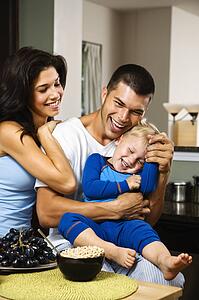 Family with toddler son in kitchen at breakfast smiling and tickling