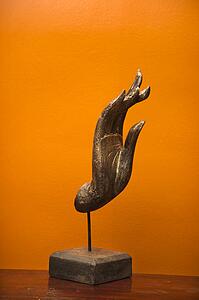 Carved hand sculpture from Thailand against orange wall.