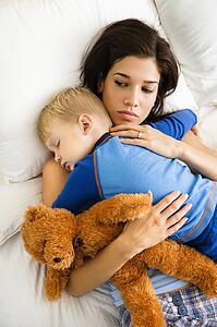 Woman holding sleeping toddler in bed 