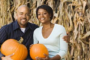 Happy smiling couple sitting on hay bales and holding pumpkins