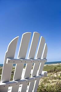 Empty white adirondack chair facing beach