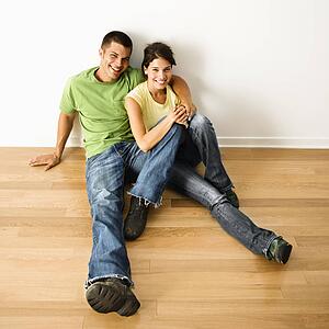 Couple sitting close on hardwood floor in home smiling