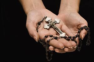 Woman's hands palm up cradling rosary with crucifix.