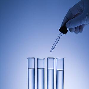 Hand holding dropper over test tubes.