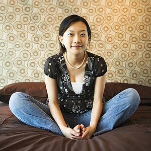 Portrait of Asian female sitting on bed looking at viewer.