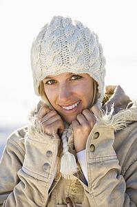 Woman in winter attire holding collar and smiling at viewer.
