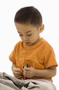 Asian boy sitting with handful of crayons.