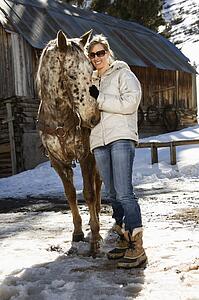 Young woman petting horse with stable in background in winter