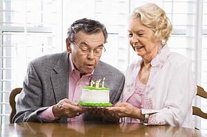 Man blowing candles out on birthday cake while woman watches