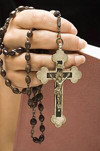 Holding Holy Bible open with rosary and crucifix in hand