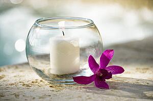 Lit candle in glass bowl and purple orchid beside pool