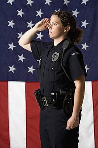 Portrait of mid adult Caucasian policewoman saluting with American flag as backdrop.