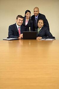 Businesspeople gathered around laptop computer smiling