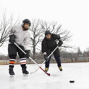 Two boys in ice hockey uniforms playing hockey on ice rink.