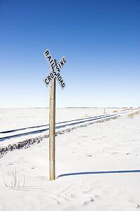 Railroad crossing sign by tracks in rural desolate snowy landscape.