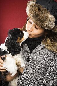 Adult woman in winter outerwear kissing a dog.