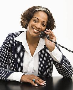Businesswoman sitting at desk holding telephone receiver to ear smiling