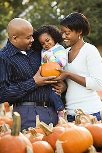 Parents and daughter picking out pumpkin and smiling at outdoor market