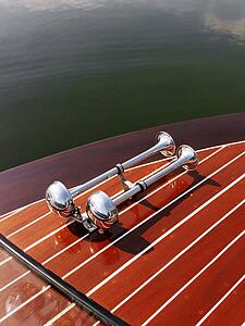 Detail of dual chrome trumpet horn on wooden boat floating in water.