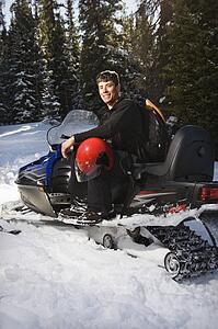 Sitting on snowmobile in snow with helmet on lap smiling