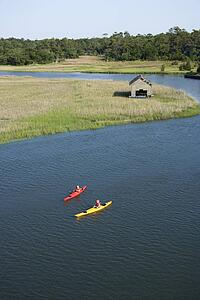 Aerial of two teenage boys kayaking through marshland on Bald Head Island, North Carolina.