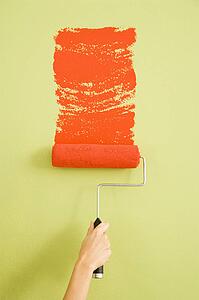 Hand painting a green wall with a red paint roller