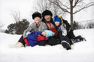 Portrait of happy family of four sitting in snow smiling at viewer