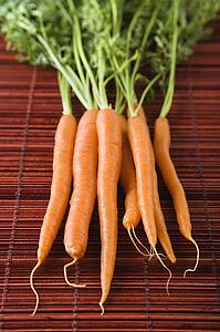 Close up of orange carrots with green tops against bamboo mat.