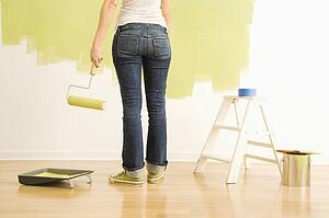 Back view of Caucasian woman holding paint roller with painting supplies.