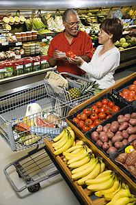 Smiling middle aged African American couple comparing produce in grocery store. 
