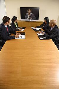 Businesspeople sitting at conference table looking at flat screen display