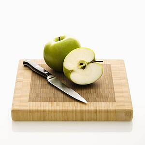 Still life of green apples and knife on cutting board.