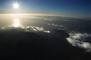 Aerial view of Maui, Hawaii coast with sun over Pacific ocean and mountainous landscape