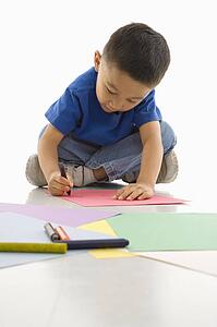 Boy sitting on floor coloring on paper