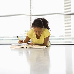 African American girl lying on floor doing homework.