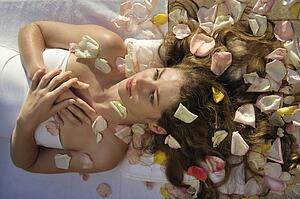 Above view of woman wrapped in sheet laying down with hair spread out on rose petals