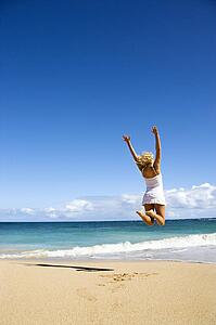 Pretty young woman jumping on Maui, Hawaii beach with arms raised into air