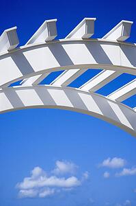 Low angle view of arched white arbor with blue sky.
