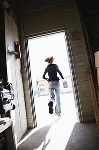 Woman running through open door from building to sunny outside.