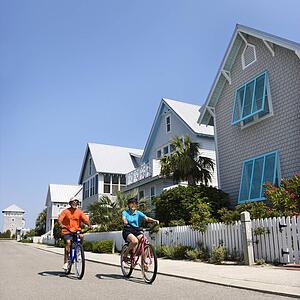 Middle aged African American couple bicycling down street next to homes and fence.