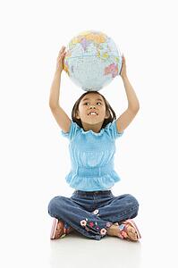 Girl sitting on floor holding Earth globe over her head