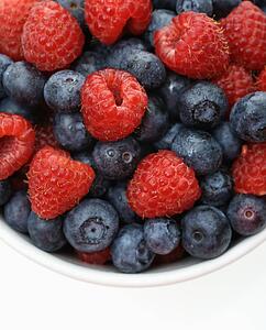 Bowl of mixed blueberries and raspberries on white background.